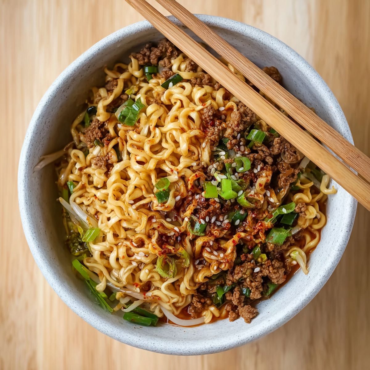 Ramen noodles bowl with ground meat, green onions, sesame seeds, and chopsticks in ceramic bowl showing upgraded instant noodles