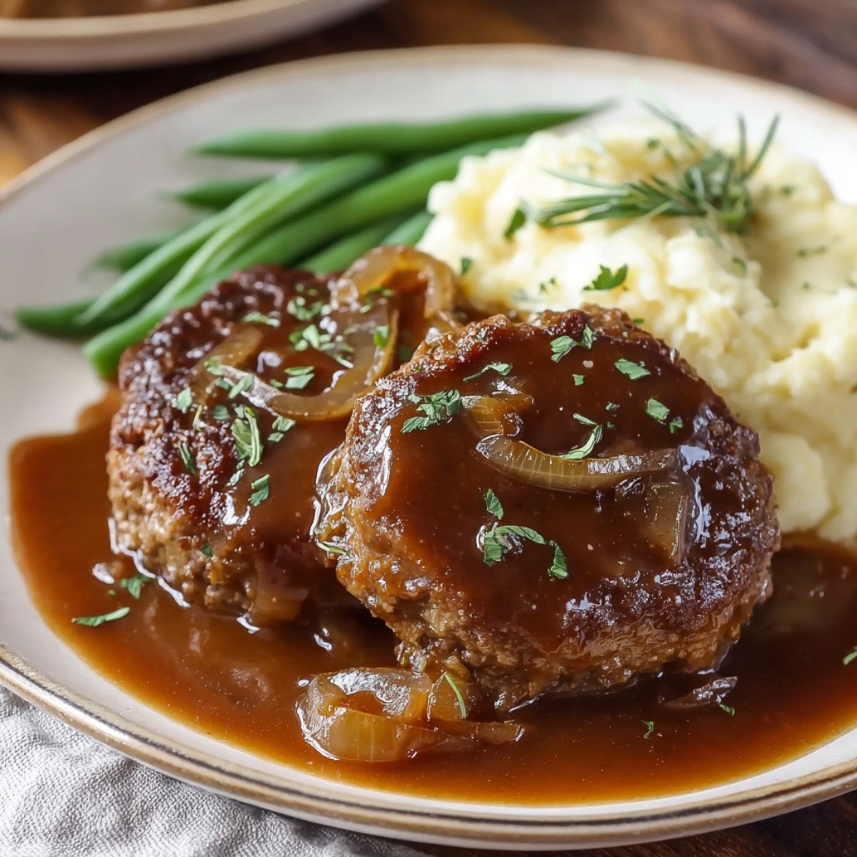 Salisbury steak recipe. A top-down shot of a plate with two Salisbury steak patties covered in mushroom gravy and onions, served with mashed potatoes and green beans. The image is split, with the top half showing a close-up and the bottom half showing the full plate with text overlay that reads "BEST EVER SALISBURY STEAK RECIPE" and a website URL.