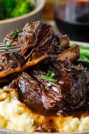 Short ribs recipe braised beef with dark rich sauce over creamy mashed potatoes and fresh green vegetables