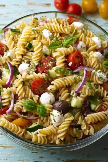 Zesty italian pasta salad overhead view showing fusilli pasta with cherry tomatoes fresh mozzarella black olives red onion and basil in glass bowl