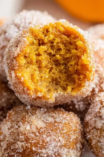Cinnamon sugar pumpkin donut holes with one broken open showing bright orange fluffy interior and generous cinnamon sugar coating piled together