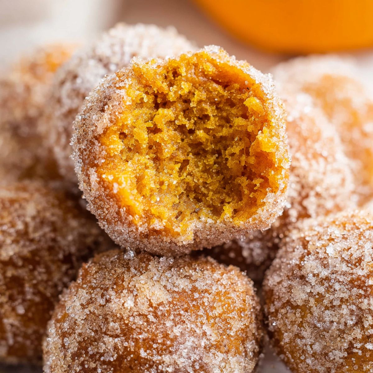 Cinnamon sugar pumpkin donut holes with one broken open showing bright orange fluffy interior and generous cinnamon sugar coating piled together