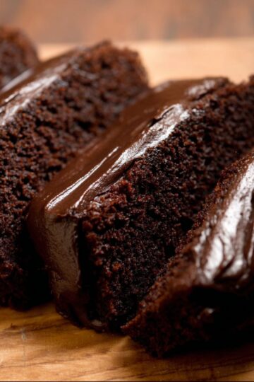 Chocolate pumpkin bread sliced on wooden board showing ultra moist dark chocolate crumb with glossy chocolate ganache topping and pumpkin in background