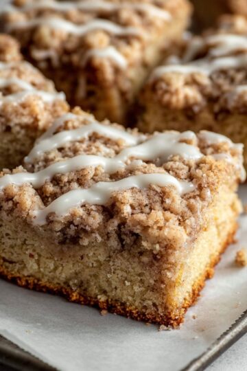 Apple cider coffee cake cut into squares showing moist tender crumb texture with generous cinnamon streusel and white glaze on metal pan