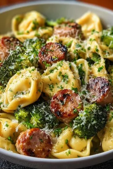 Garlic parmesan tortellini with sausage and broccoli in white bowl showing cheese-filled tortellini, crispy Italian sausage slices, tender broccoli florets topped with grated parmesan cheese and fresh parsley