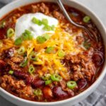 Homemade beef and bean chili recipe with sour cream, cheddar cheese, and green onions.