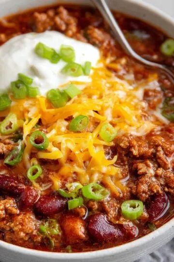Homemade beef and bean chili recipe with sour cream, cheddar cheese, and green onions.