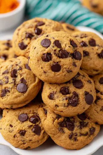 Pumpkin chocolate chip cookies stacked on white plate showing soft thick texture with chocolate chips and golden pumpkin color