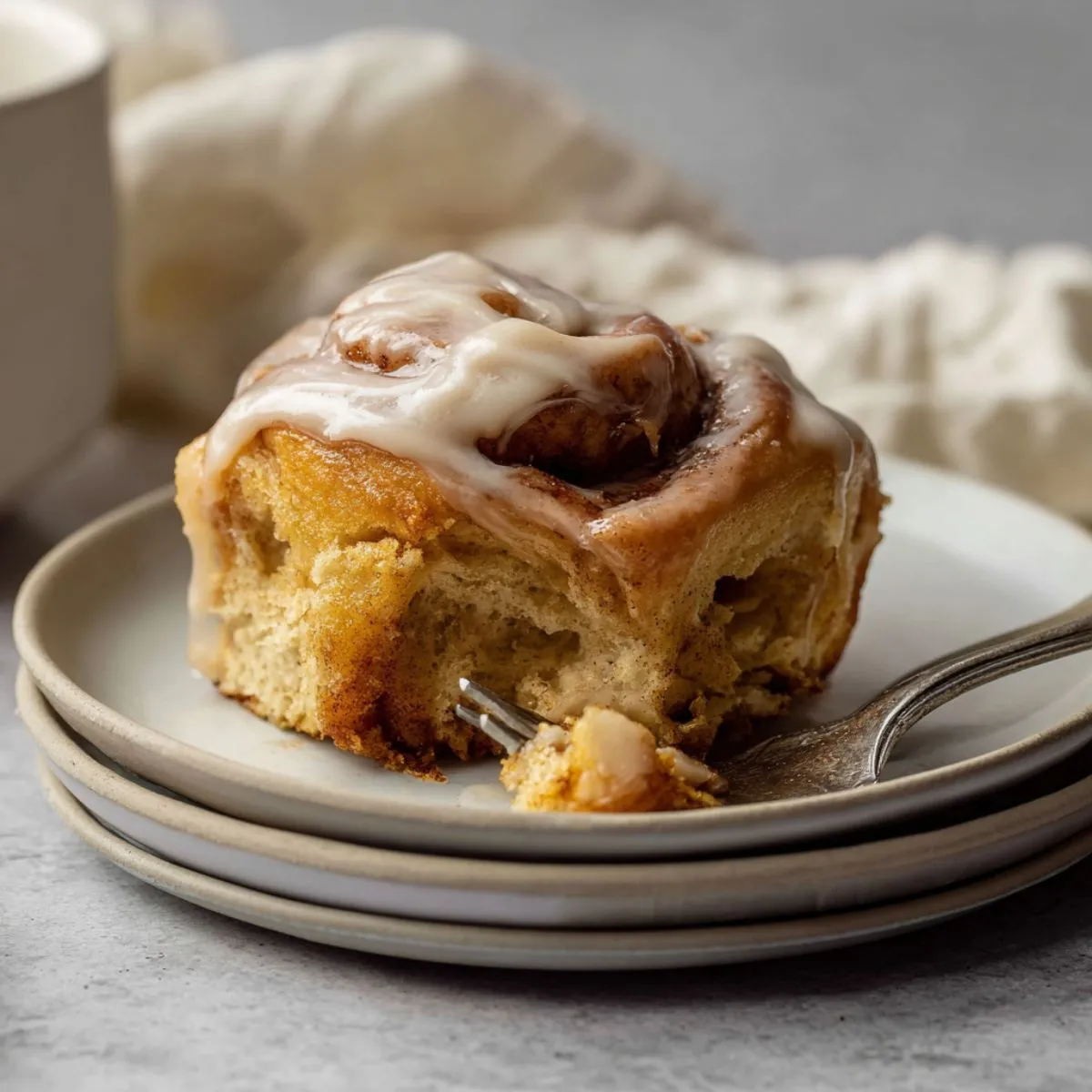 Pumpkin cinnamon rolls with cream cheese frosting on white plate showing soft fluffy layers with cinnamon swirls and glaze dripping down sides with fork taking bite
