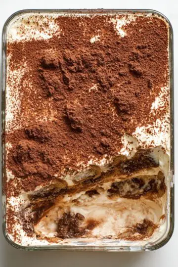 Tiramisu chia pudding in glass dish with layers of coffee-soaked chia, mascarpone cream, and cocoa powder dusting with spoon marks