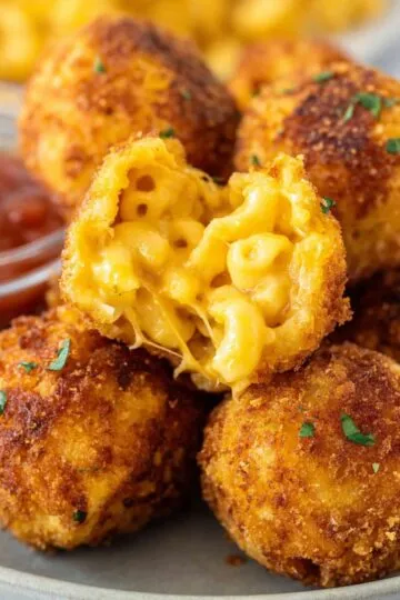 Fried mac and cheese balls on a white plate with one cut open revealing creamy macaroni and cheese with melted cheese pull