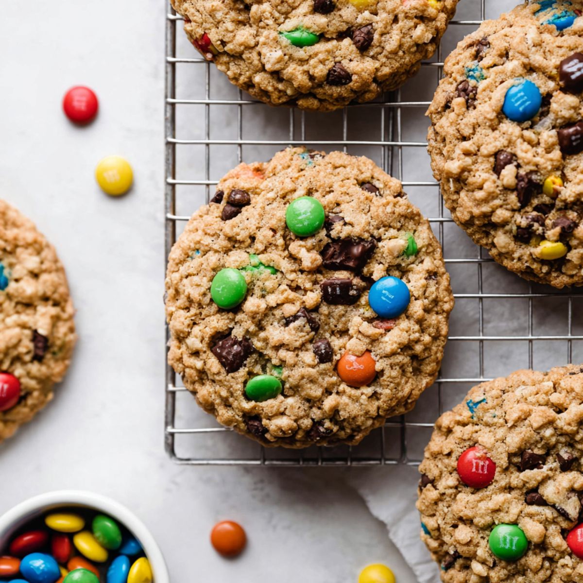 Jumbo monster cookies recipe on cooling rack with M&Ms, chocolate chips, oatmeal texture, and scattered candies showing soft chewy centers