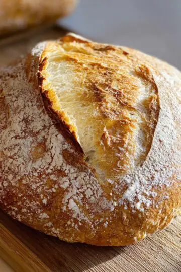 Sourdough bread artisan round loaf with decorative leaf scoring pattern, golden brown crust, flour dusting on wooden board in natural lighting