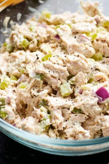 Tuna salad recipe with flaked tuna, diced celery, and red onion mixed with mayo in a clear glass bowl