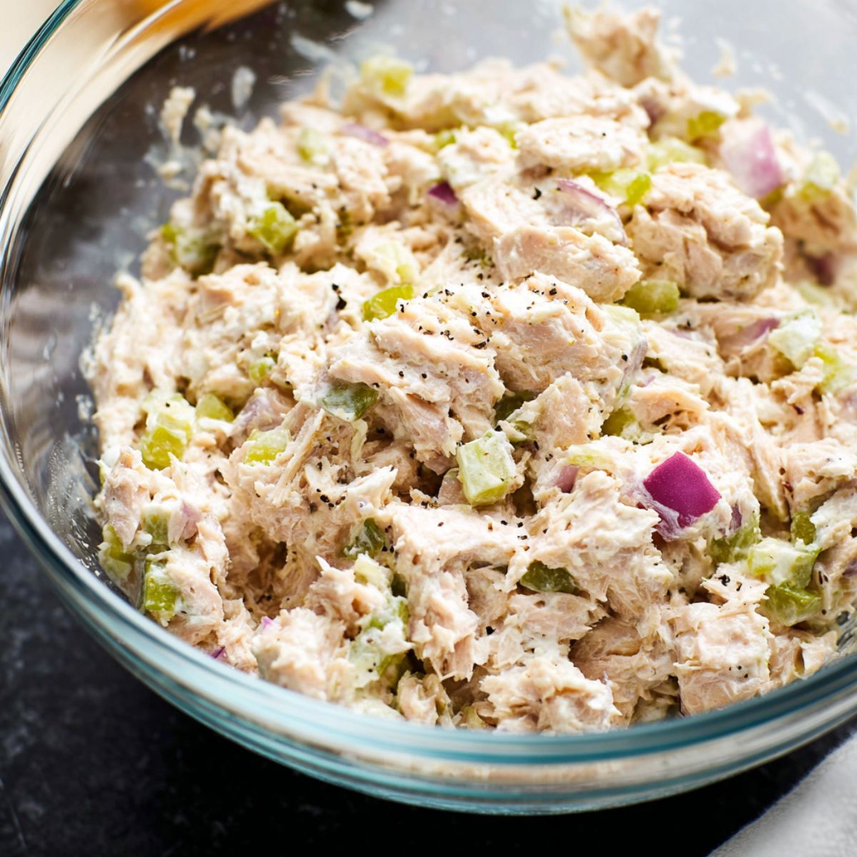 Tuna salad recipe with flaked tuna, diced celery, and red onion mixed with mayo in a clear glass bowl