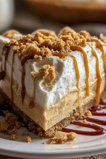 Butterscotch heaven pie slice with tall whipped cream topping drizzled with butterscotch sauce and graham cracker crumb garnish on white plate showing layers of creamy filling and golden crust