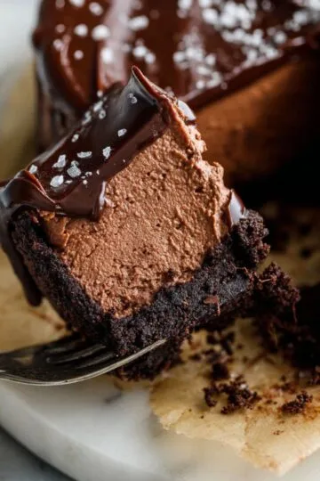Fork holding a bite of dense chocolate cheesecake with a brownie crust.