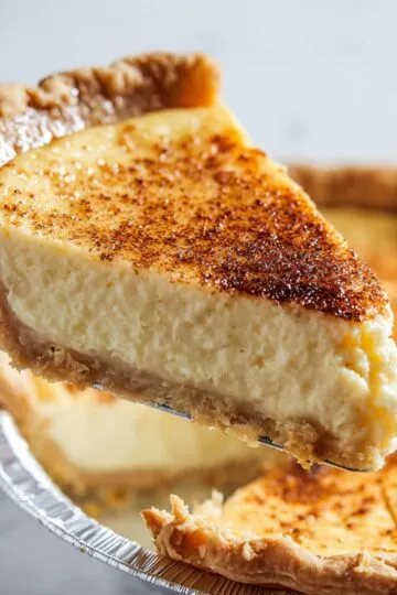 Egg custard pie slice being lifted on server showing thick creamy custard filling, flaky crust, caramelized nutmeg spice on top