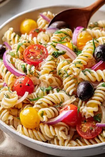 Close view of cooked rotini pasta tossed with glossy black olives and red onions.