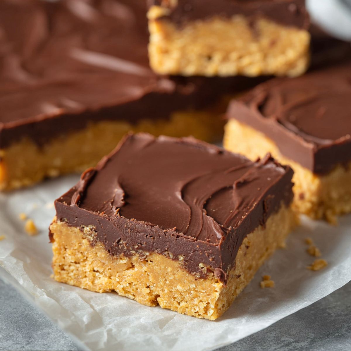 Protein bars with chocolate topping and peanut butter oat base on parchment paper showing chewy homemade texture