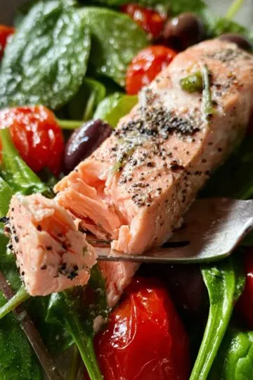 Silver fork flaking a piece of juicy roasted salmon served with green beans.