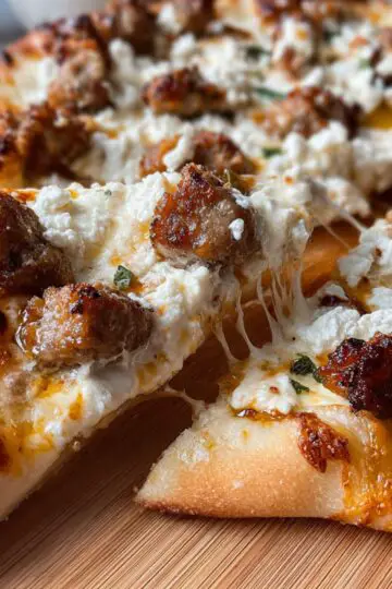 Close-up of a sausage feta honey pizza slice being lifted with stretchy cheese.