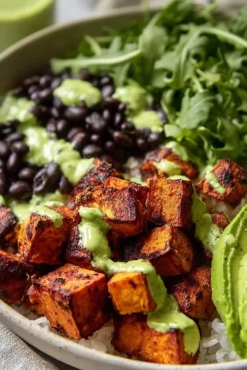 Close-up of roasted sweet potatoes and sliced avocado served in a rice bowl.