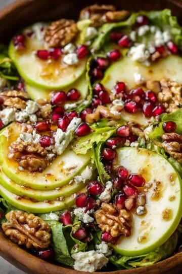 Winter salad in wooden bowl with sliced pears, pomegranate seeds, candied walnuts, goat cheese crumbles, mixed greens, festive holiday side dish