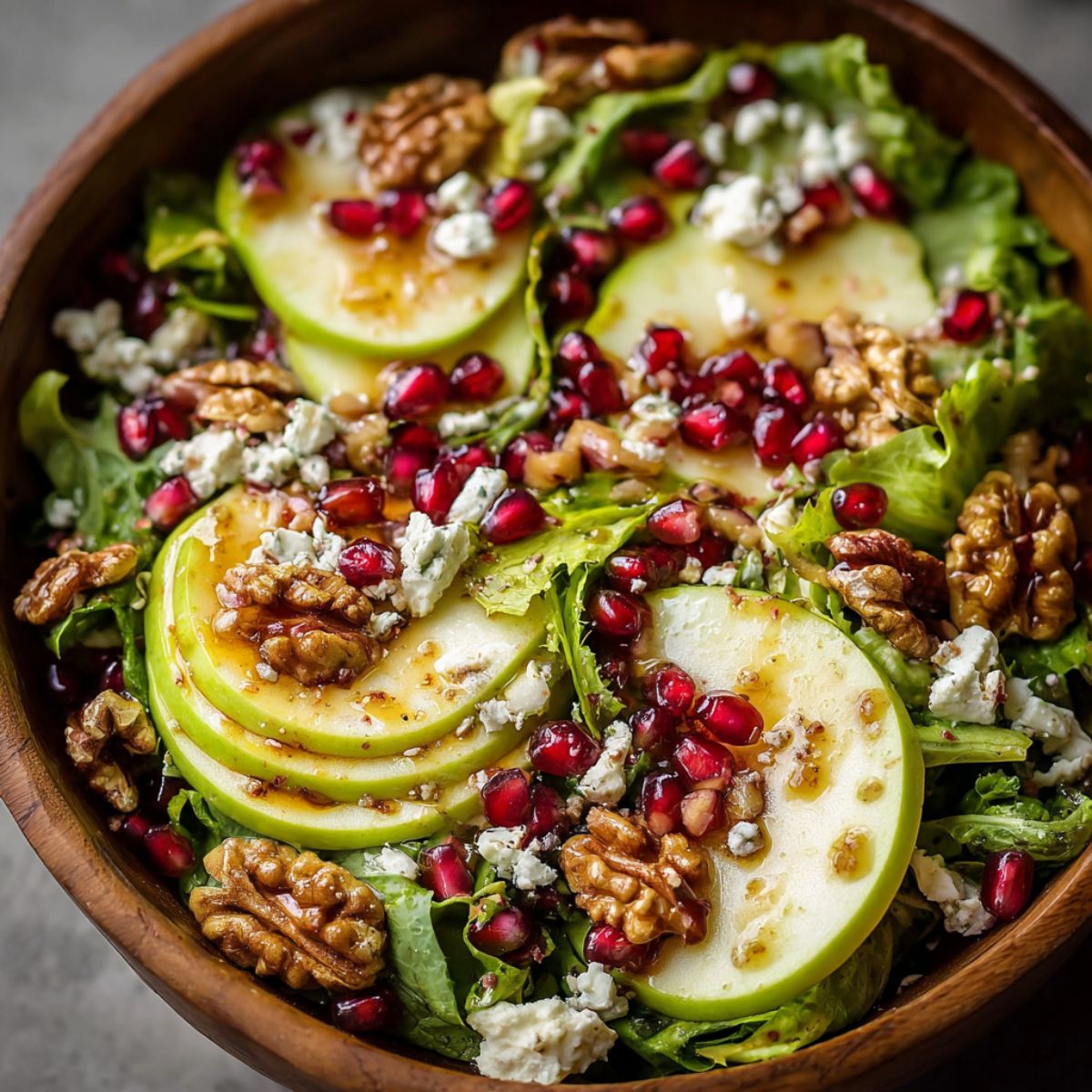 Winter salad in wooden bowl with sliced pears, pomegranate seeds, candied walnuts, goat cheese crumbles, mixed greens, festive holiday side dish