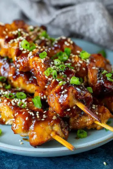 Stack of grilled yakitori chicken skewers garnished with sesame seeds and green onions.