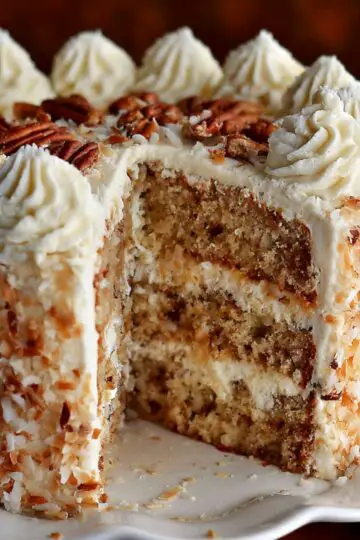 Sliced whole bavarian cream cake on a white stand topped with whipped cream and pecans.