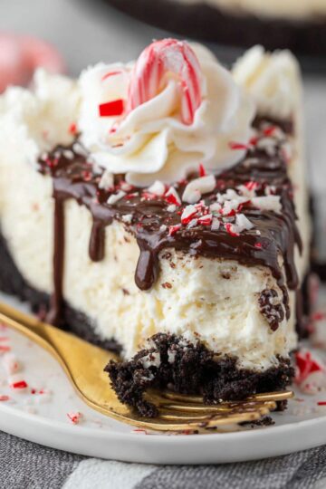 Sliced white chocolate cheesecake topped with chocolate glaze and crushed peppermint candy.