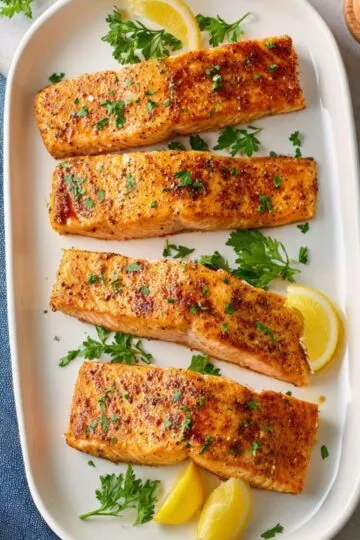 Golden brown air fryer salmon fillets topped with chopped herbs and served with citrus slices.