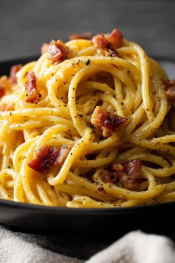 Bacon Carbonara Pasta 7 A warm bowl of Bacon Carbonara Pasta covered in shiny sauce and pepper.