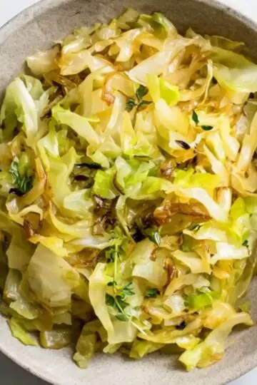 Easy Cabbage Recipe 5 A ceramic bowl filled with glossy Cabbage Recipe garnished with fresh green thyme.