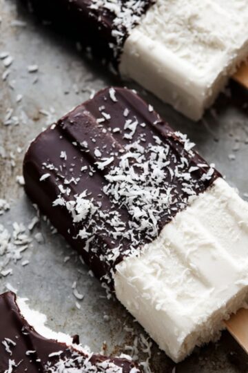 Frozen coconut ice cream bars resting on a cold metal tray with scattered flakes.