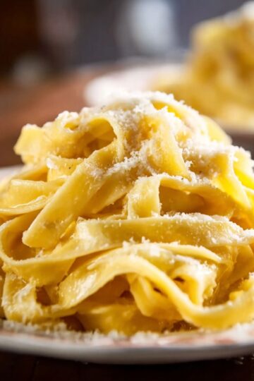 Mound of hot fettuccine alfredo coated in glossy cheese sauce and black pepper.