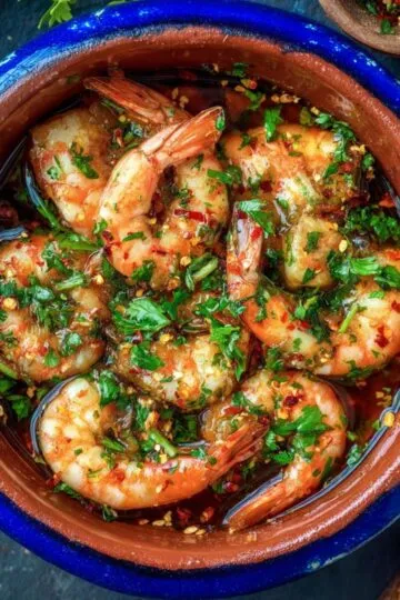 Authentic gambas al ajillo served in a rustic clay cazuela.