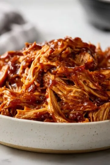 White bowl filled with steaming sticky instant pot pulled bbq chicken pieces.