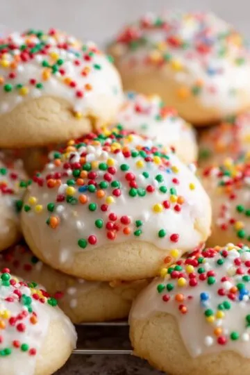 Close up of stacked Italian Ricotta Cookies featuring smooth icing and colorful nonpareil candies.