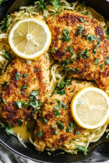 Crispy lemon chicken romano served in a cast iron pan with pasta and parsley.
