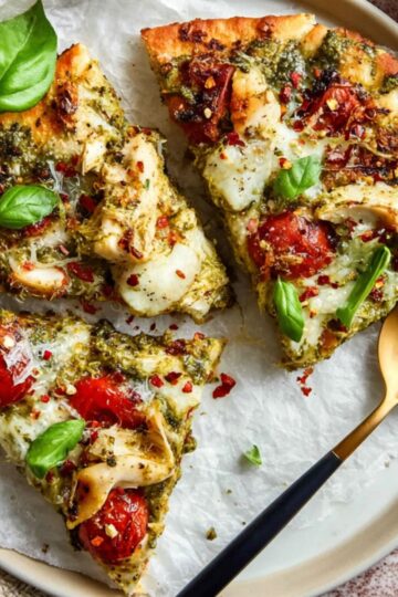Sliced pesto chicken flatbread with roasted tomatoes and fresh basil leaves on a plate.