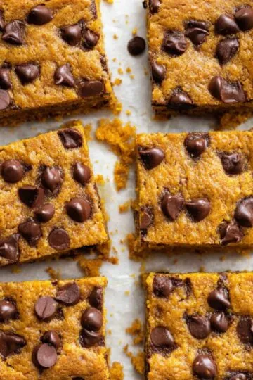 Square slices of baked pumpkin maple blondies filled with chocolate chips on parchment.