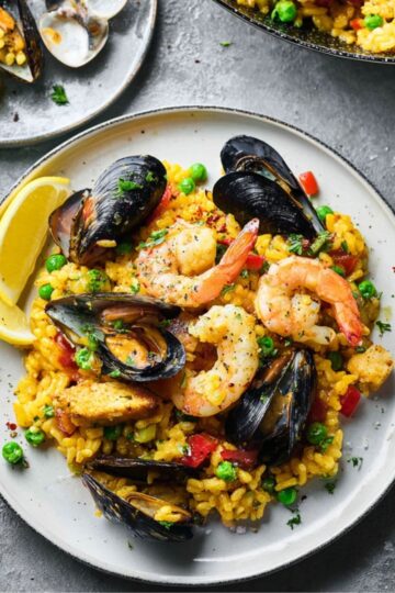 Served Spanish Paella featuring yellow saffron rice, mussels, and shrimp on grey stoneware.