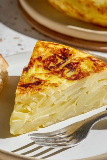 Thick Spanish tortilla slice on plate with crusty bread and fork