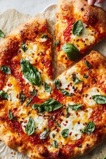 Hand lifting a hot slice of margherita pizza with melted mozzarella cheese.