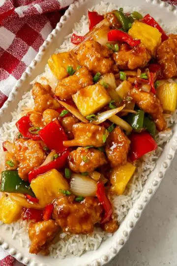 Sweet and sour chicken served over fluffy white rice on a white beaded platter.
