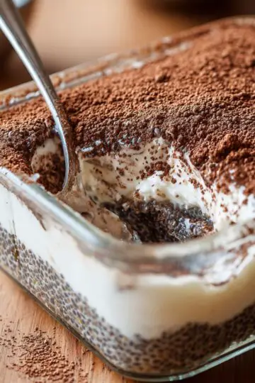 Spoon scooping into layered tiramisu chia pudding recipe topped with dark cocoa powder