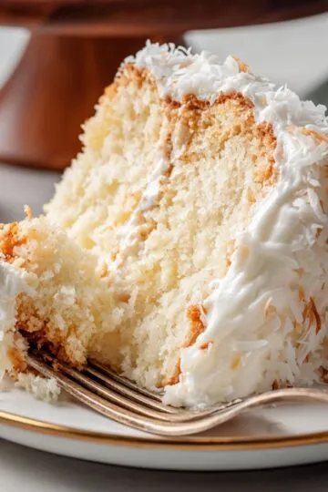 Fork cutting into tender tom cruise coconut cake slice with white frosting