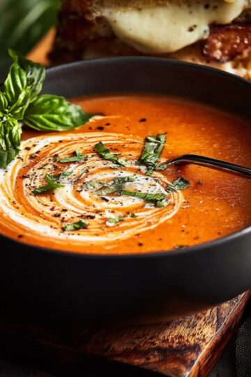 Spoon dipping into orange tomato soup topped with cream and black pepper